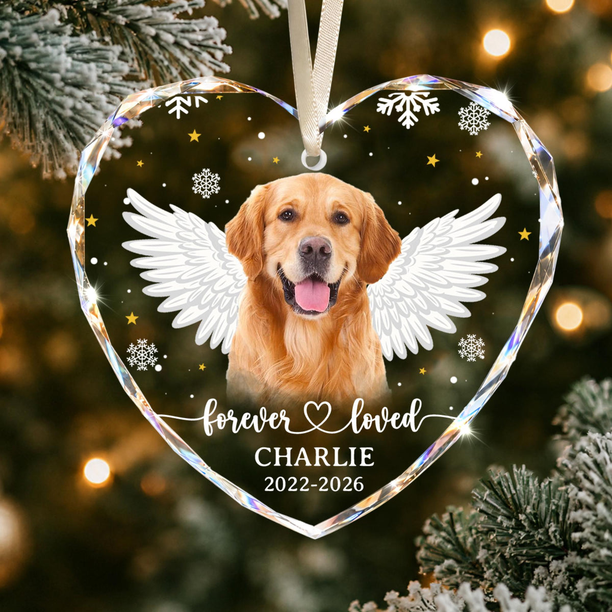 A heart-shaped glass ornament featuring a golden retriever with white angel wings, surrounded by gold stars and white snowflakes. The text reads "forever loved", "CHARLIE", and "2022-2026". It hangs from a white ribbon.