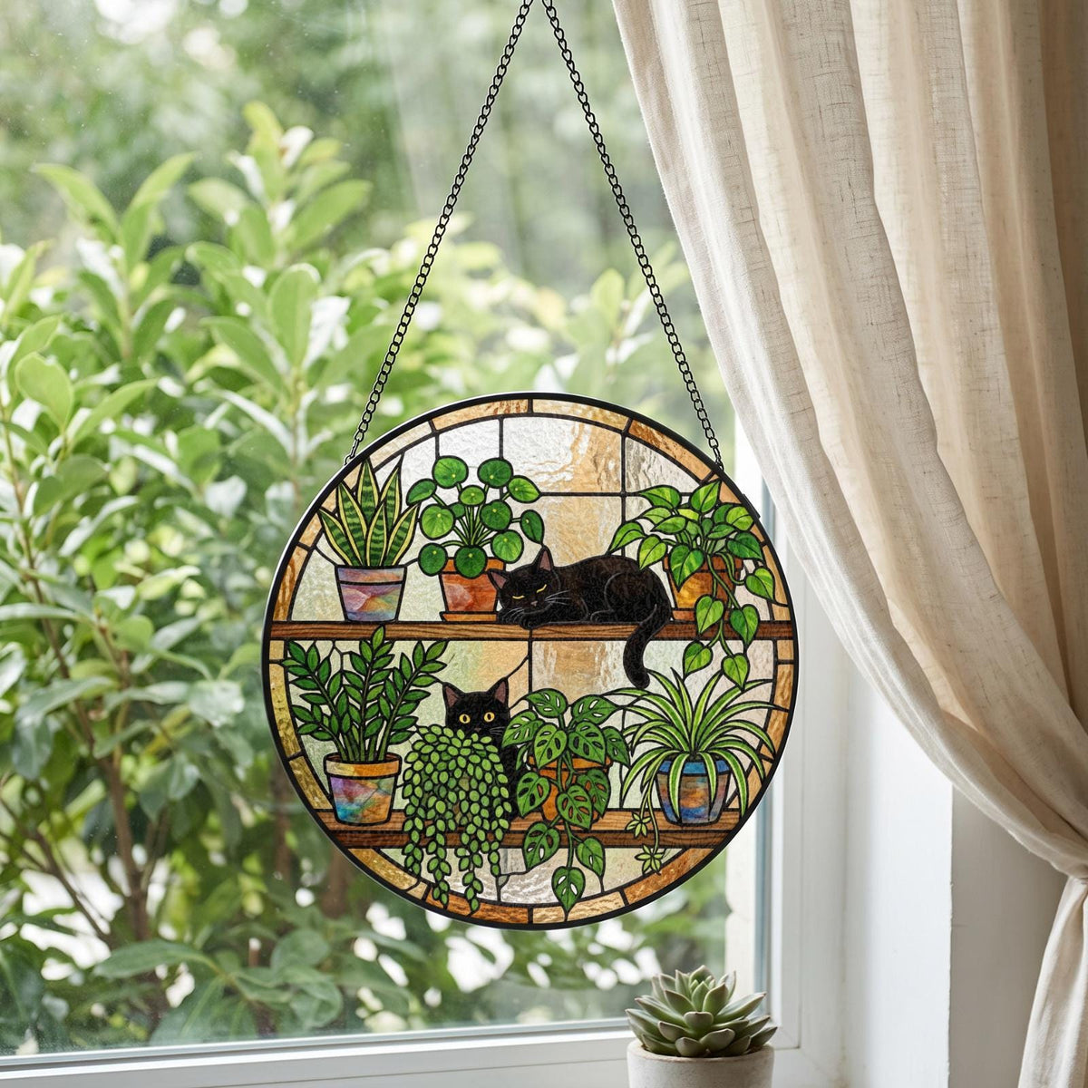 A circular stained glass suncatcher featuring two black cats resting on shelves among various potted houseplants. The design includes a snake plant, a pilea, a trailing pothos, and other green foliage in colorful pots, suspended by a black chain.
