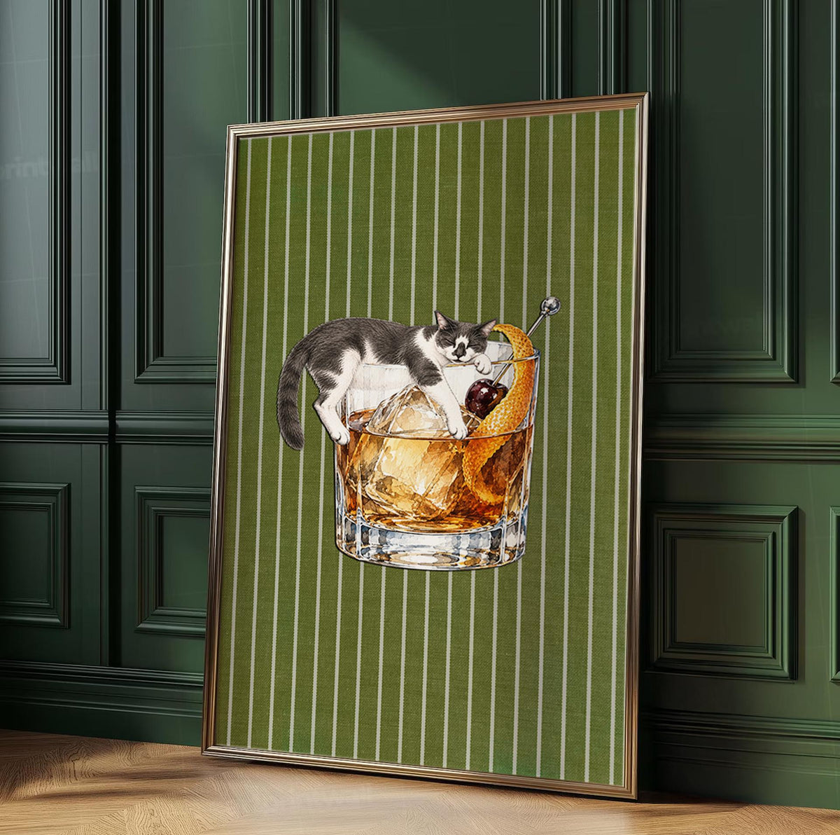 A framed wall art print featuring a grey and white cat lounging over a glass of amber-colored liquid with ice cubes, a dark red cherry, and an orange peel garnish, set against a vertical olive green background with thin white stripes.