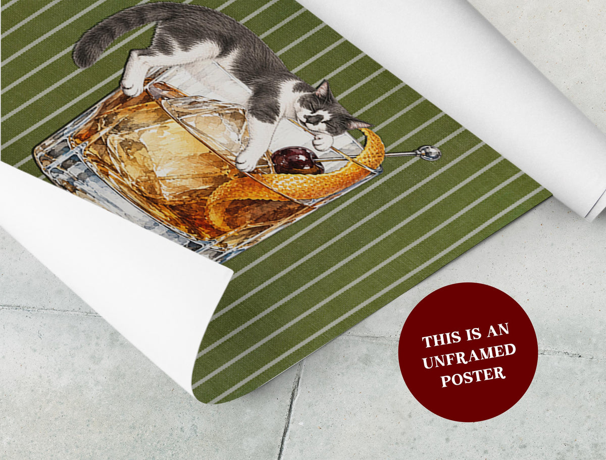 An unframed poster featuring a gray and white cat sleeping on a square glass of amber-colored liquid with ice, a dark cherry, and an orange peel garnish. The background is olive green with thin white vertical stripes. Text reads: THIS IS AN UNFRAMED POSTER.