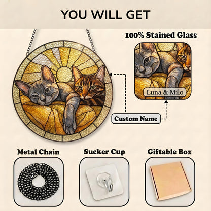 A circular stained glass suncatcher featuring two cats against a sunburst background. Includes a metal chain, a clear suction cup, and a giftable box. The glass panel displays the custom name Luna & Milo in a rectangular label.