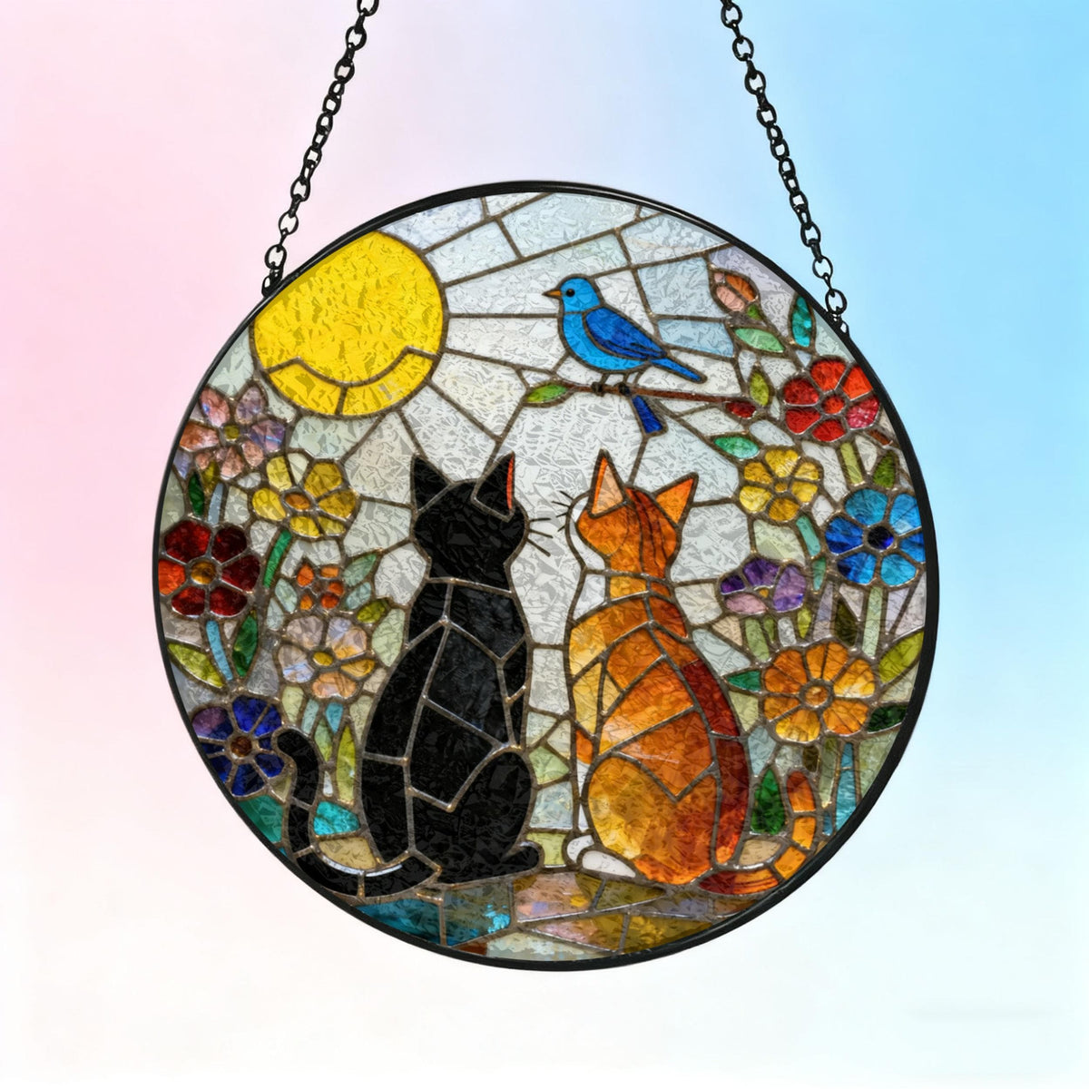 Round stained glass window art featuring two cats gazing at a blue bird perched on a branch. The scene includes a yellow sun, colorful flowers, and a black metal chain for hanging. The cats are black and orange.
