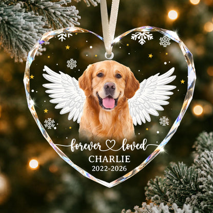 A heart-shaped glass ornament featuring a golden retriever with white angel wings, surrounded by gold stars and white snowflakes. The text reads "forever loved", "CHARLIE", and "2022-2026". It hangs from a white ribbon.