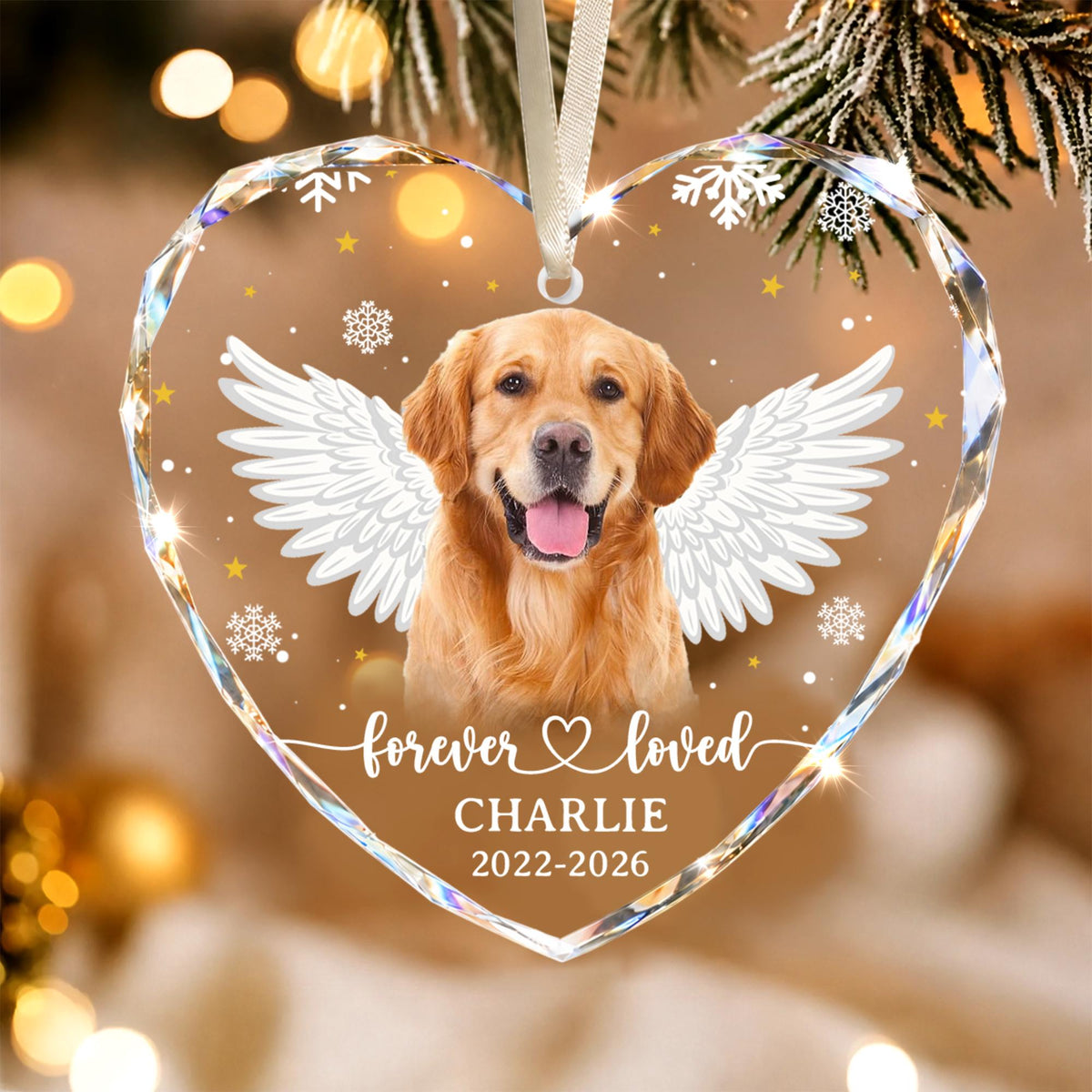 A heart-shaped clear acrylic ornament featuring a golden retriever with white angel wings. The text reads "forever loved", "CHARLIE", and "2022-2026". The design includes white snowflakes and small yellow stars, suspended by a white ribbon.