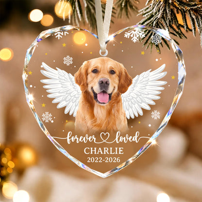 A heart-shaped clear acrylic ornament featuring a golden retriever with white angel wings. The text reads "forever loved", "CHARLIE", and "2022-2026". The design includes white snowflakes and small yellow stars, suspended by a white ribbon.