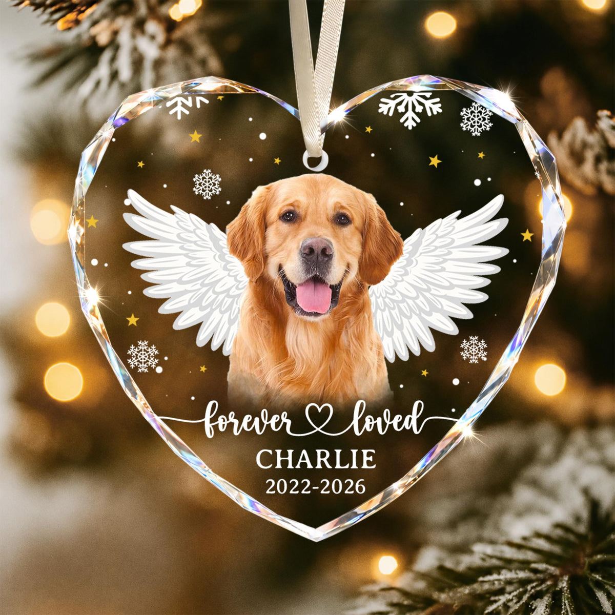 A heart-shaped clear acrylic ornament featuring a golden retriever with white angel wings. The text reads "forever loved", "CHARLIE", and "2022-2026". The design includes white snowflakes and small yellow stars, suspended by a white ribbon.