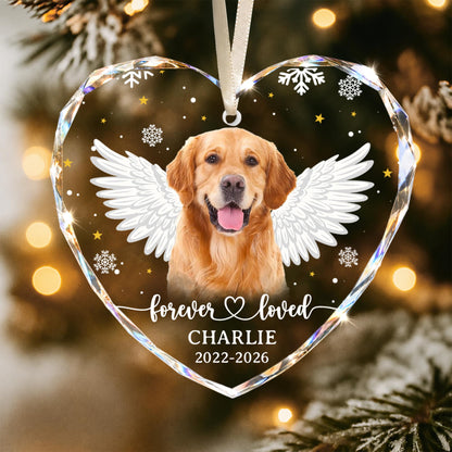 A heart-shaped clear acrylic ornament featuring a golden retriever with white angel wings. The text reads "forever loved", "CHARLIE", and "2022-2026". The design includes white snowflakes and small yellow stars, suspended by a white ribbon.