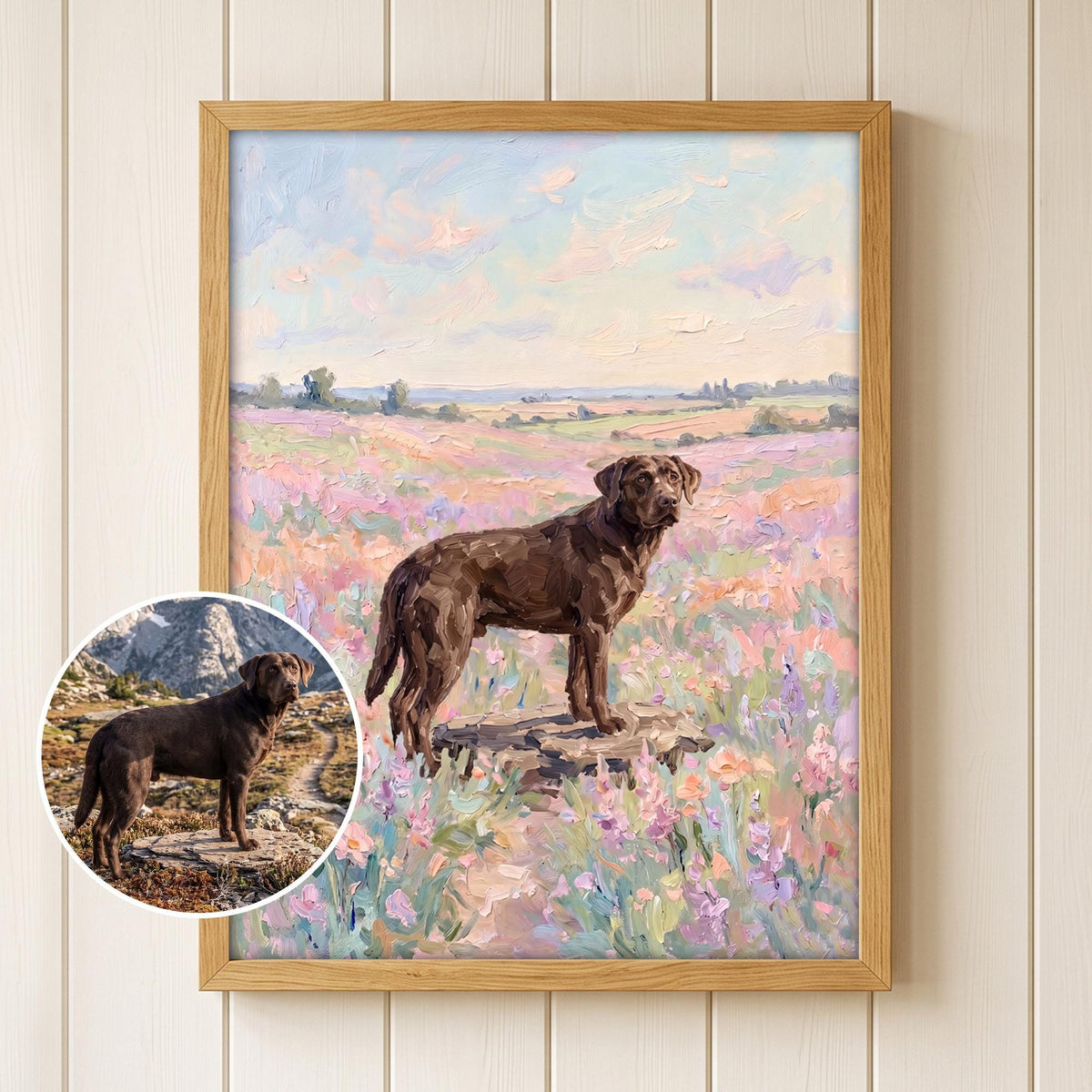 A framed oil painting depicting a brown Labrador retriever standing on a rock in a field of pink and purple wildflowers under a soft pastel sky. A circular inset shows the original photograph of the dog in a mountain landscape.