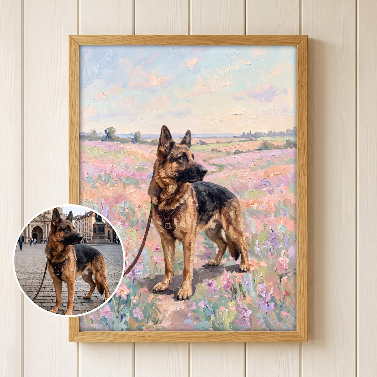 A framed oil painting of a German Shepherd dog wearing a black harness and leash, standing in a field of pink and purple flowers under a soft sky. A circular inset shows the original photograph of the same dog in a city square.