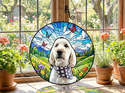 Round stained glass window featuring a dog with a black and white bandana. The background is a colorful landscape with butterflies, mountains, and a blue sky. The window hangs from a chain.