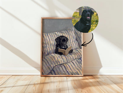 A framed rectangular print featuring a painting of a black Labrador retriever lying on a striped pillow while holding an open book. A circular inset at the top right shows a photograph of the same black dog in a grassy outdoor setting.