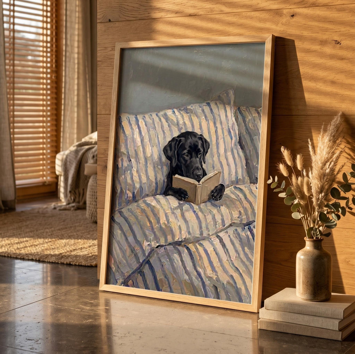A framed wall art print featuring a black Labrador retriever sitting on a blue and white striped sofa while holding an open book. The dog is positioned in the center of the composition, looking down at the pages of the book.