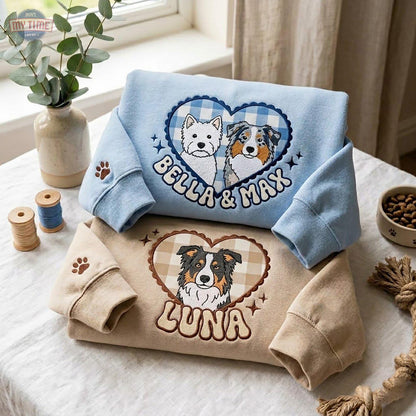 A light blue sweatshirt featuring an embroidered heart with a blue gingham pattern, two dogs, and the text "BELLA & MAX". Below it, a tan sweatshirt features an embroidered heart with a tan gingham pattern, one dog, and the text "LUNA".