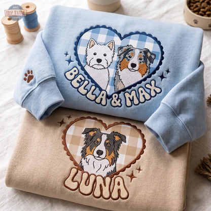 A light blue sweatshirt featuring an embroidered heart with a blue gingham pattern, two dogs, and the text 'BELLA & MAX'. Below it, a tan sweatshirt displays an embroidered heart with a tan gingham pattern, one dog, and the text 'LUNA'.