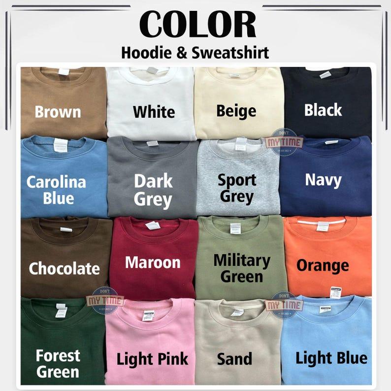 A color chart for hoodies and sweatshirts featuring fifteen folded garments in various shades including brown, white, beige, black, Carolina blue, dark grey, sport grey, navy, chocolate, maroon, military green, orange, forest green, light pink, sand, and light blue.