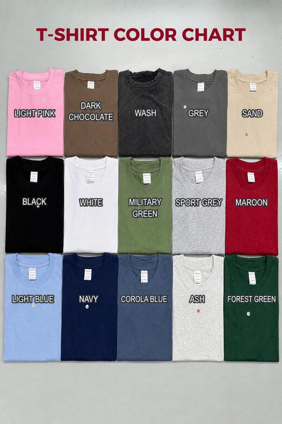 A T-shirt color chart displaying fifteen folded crew neck shirts in various colors including light pink, dark chocolate, wash, grey, sand, black, white, military green, sport grey, maroon, light blue, navy, corola blue, ash, and forest green.