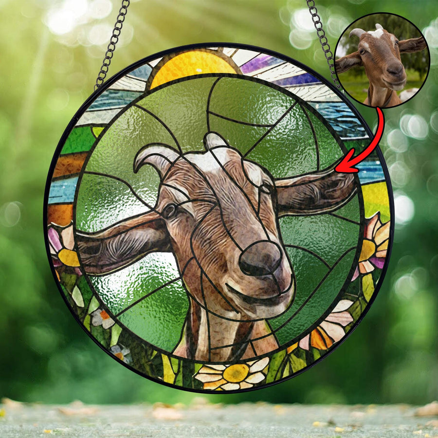 A stained glass window hanging with a colorful design featuring a goat with brown and white fur. The goat is surrounded by flowers and a sun in the background.
