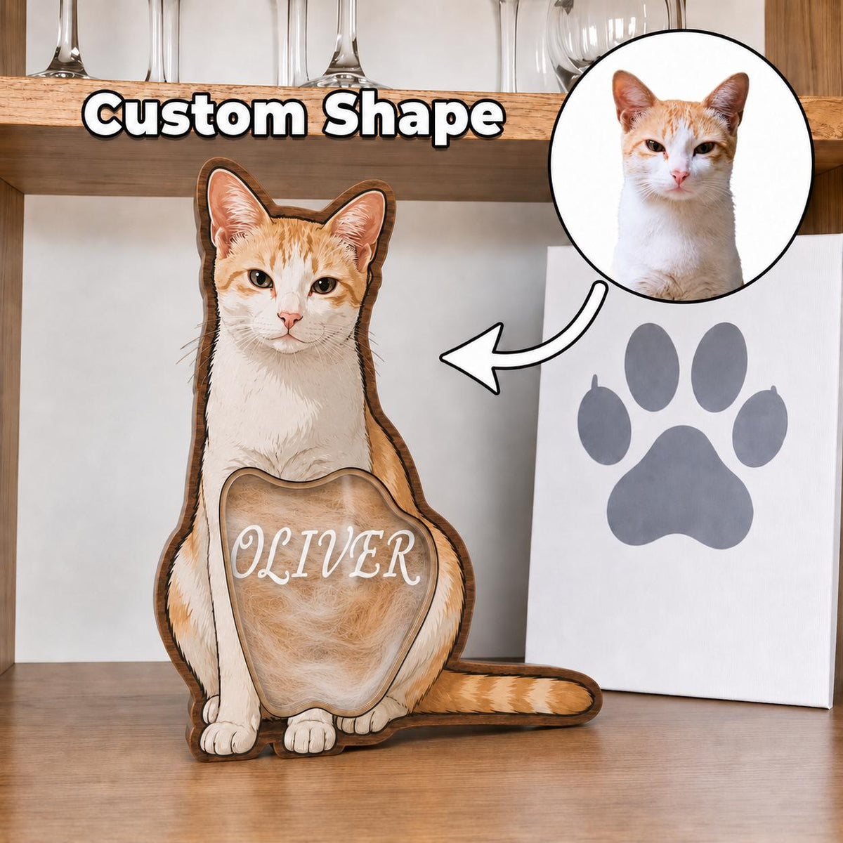 A custom-shaped wooden cat-shaped shadow box featuring an illustration of an orange and white cat with the name OLIVER printed in white on a clear front panel. A circular inset shows a photograph of the same orange and white cat.