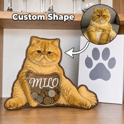 A custom-shaped wooden coin bank featuring a printed orange cat with the name Milo written in white script across a clear acrylic window filled with various metal coins. The design is based on a circular photo of an orange cat.