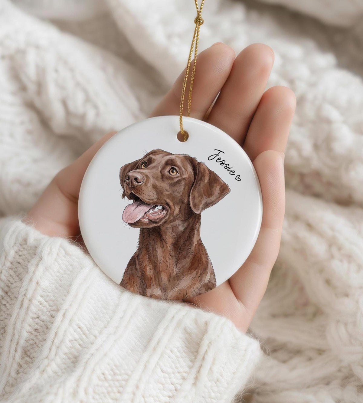A round white ceramic ornament featuring a detailed illustration of a brown Labrador retriever with its tongue out. The name Jessie is printed in black script next to a small heart symbol. A thin gold string is attached to the top.