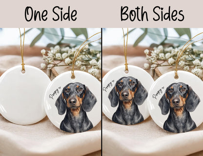 A round white ceramic ornament featuring a black and tan dachshund illustration with the text Poopy and a small heart. The ornament hangs from a gold string. The image displays two options: one side printed or both sides printed.