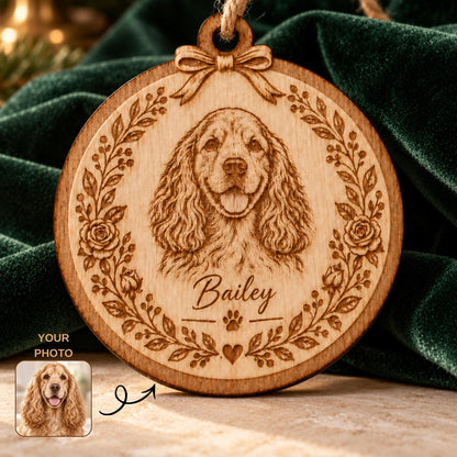 A round wooden ornament featuring a laser-engraved portrait of a spaniel dog surrounded by a floral wreath. The name Bailey is engraved below the dog, followed by a paw print and a heart. A small bow is carved at the top with a jute string.