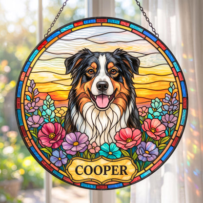 A circular stained glass suncatcher featuring a black, white, and tan Australian Shepherd dog centered against a sunset background. The dog is surrounded by colorful flowers, and a plaque at the bottom displays the name COOPER.