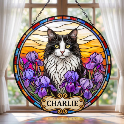 A circular stained glass suncatcher featuring a black and white cat with yellow eyes surrounded by purple iris flowers. The background shows a sunset sky with orange and yellow hues. A decorative plaque at the bottom reads CHARLIE.