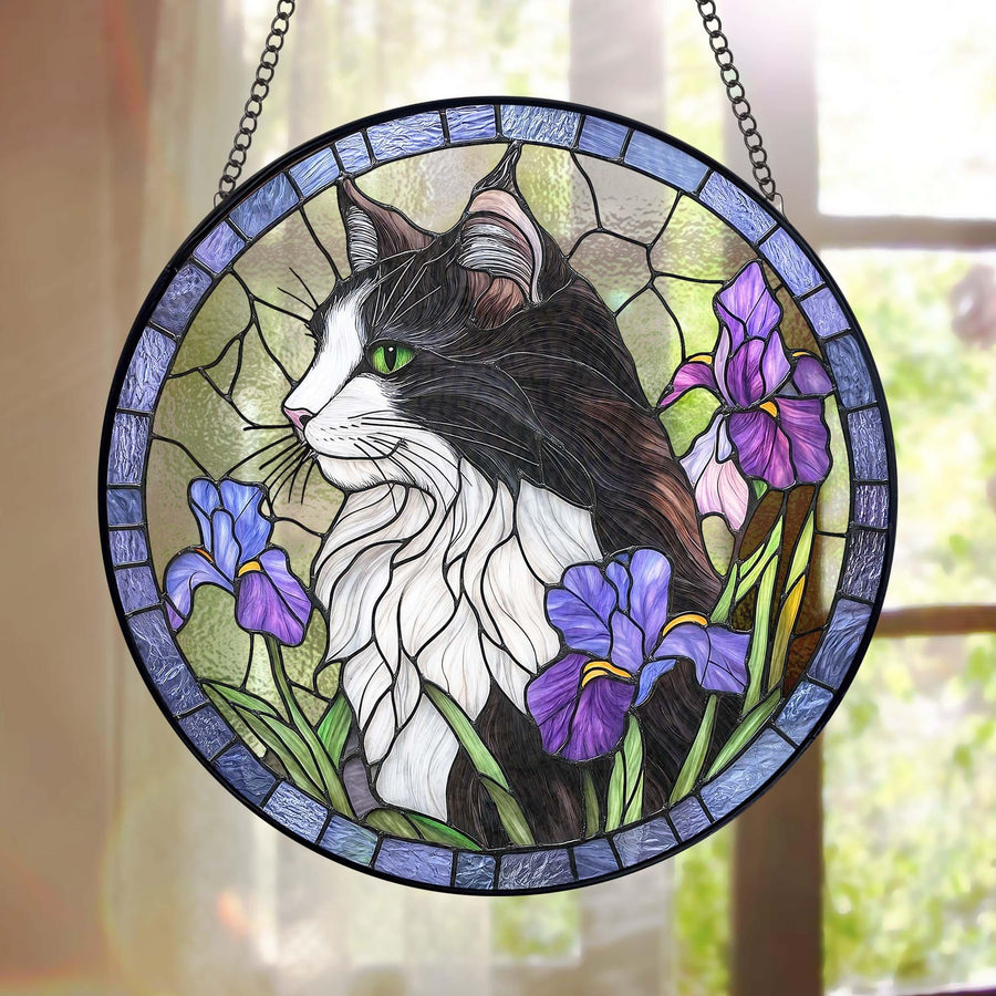 Round stained glass window featuring a black and white cat with green eyes, surrounded by purple irises. The cat is set against a light green background, framed by a blue border and a black chain for hanging.