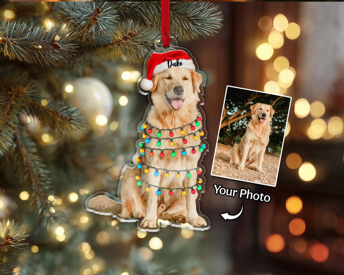A clear acrylic Christmas ornament featuring a golden retriever wearing a Santa hat and string lights. The ornament includes a photo and the name "Duke". The words "Your Photo" are also visible.