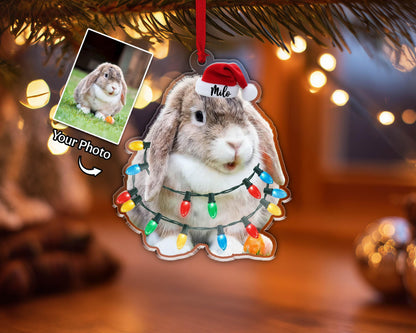 A Christmas ornament featuring a rabbit wearing a Santa hat with the name "Milo" and a string of colorful Christmas lights. The ornament has a photo of a rabbit on the left side with the text "Your Photo".