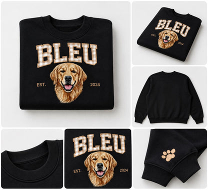 A black crewneck sweatshirt featuring a graphic of a golden retriever's face. Above the dog, the word BLEU is printed in a beige and white gingham pattern. The text EST. and 2024 flank the dog. A small beige paw print is on the sleeve.