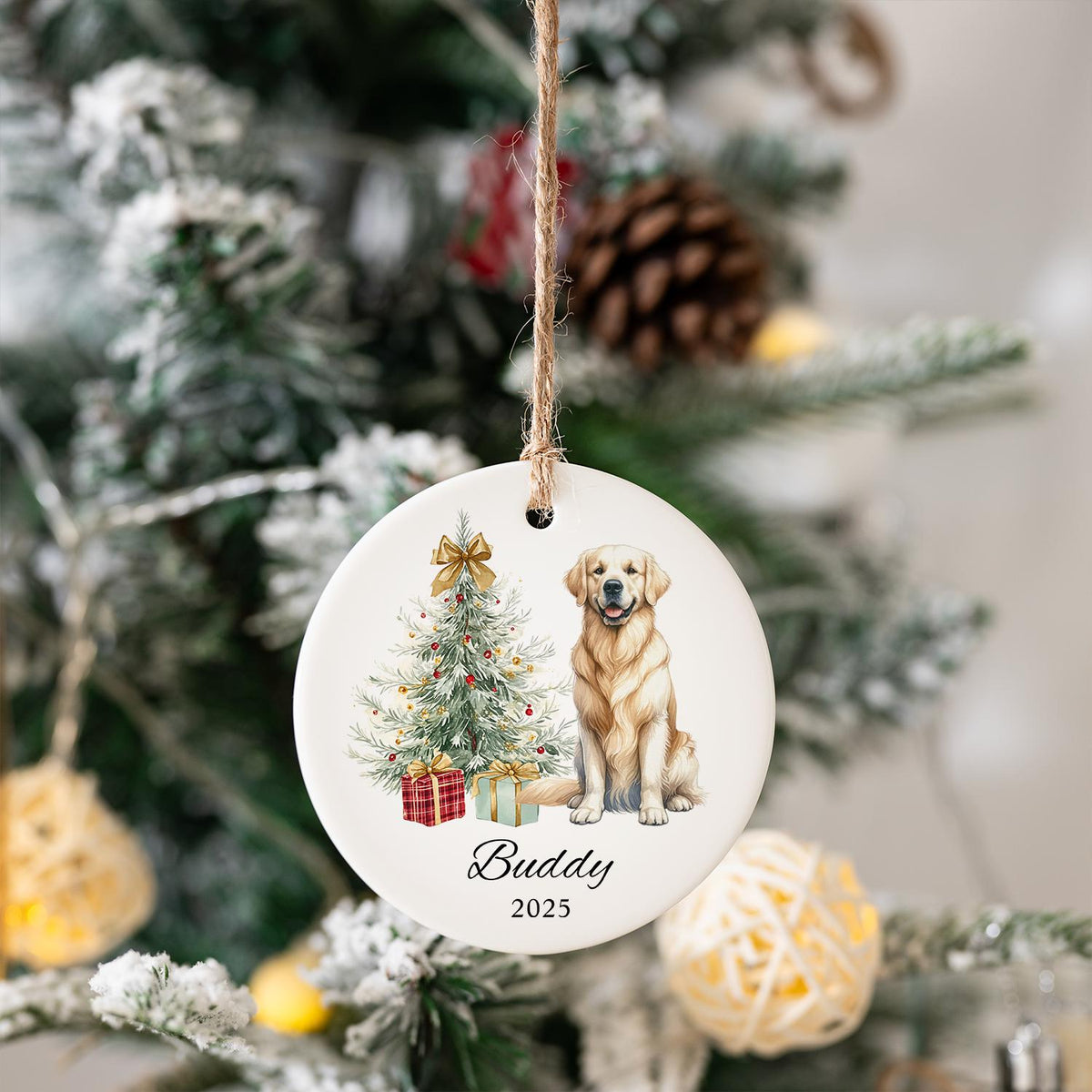 A round, white Christmas ornament with a watercolor illustration of a golden retriever, Christmas tree, and gifts. The ornament has the name "Buddy" and the year "2025" printed on it. A jute string is attached for hanging.