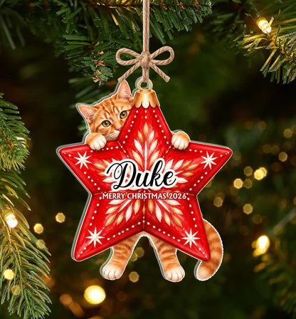 A star-shaped Christmas ornament featuring an orange tabby cat peeking over the top and holding onto the edges. The red star has a gold center pattern, white star accents, and the text Duke and MERRY CHRISTMAS 2026 printed on it.