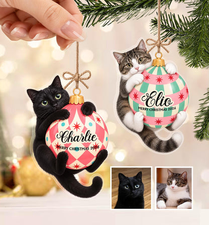 Two flat Christmas tree ornaments featuring a black cat and a tabby cat each hugging a round bauble. The black cat ornament says Charlie Merry Christmas 2026 and the tabby cat ornament says Elio Merry Christmas 2026. Both have twine loops.