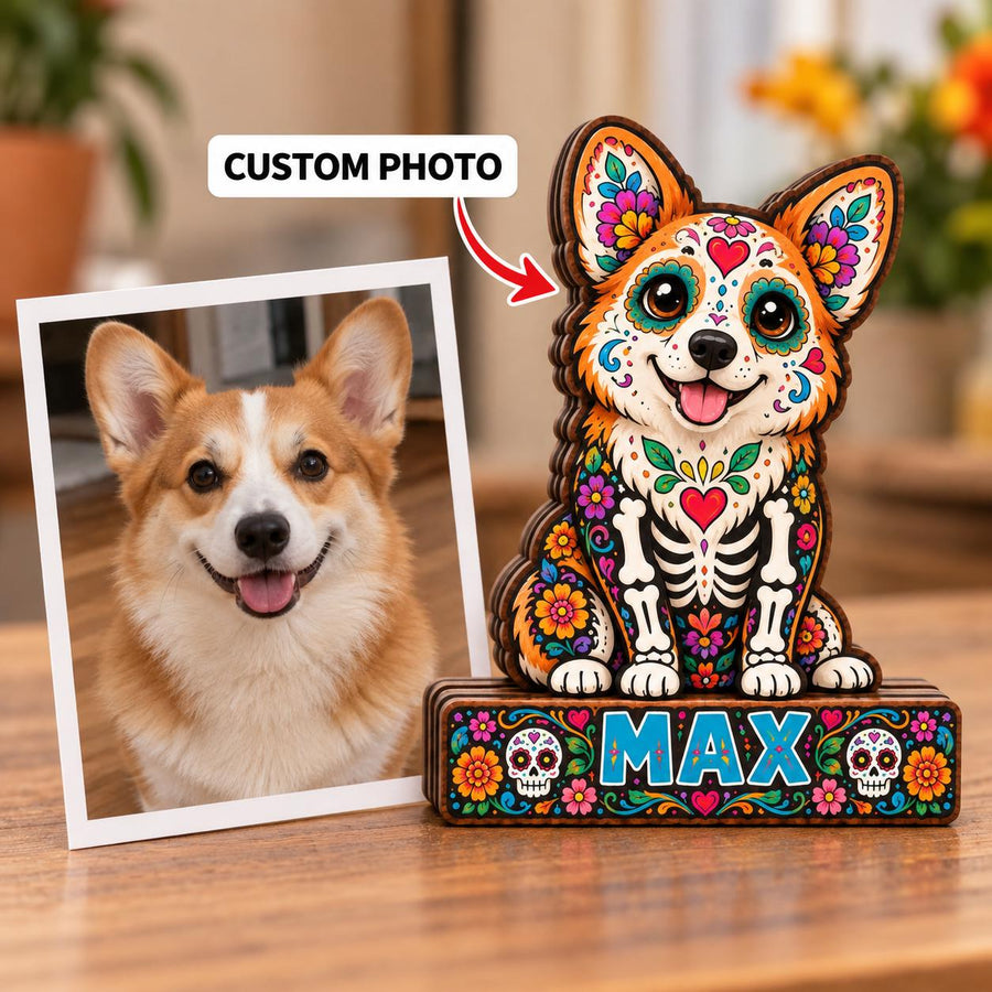 A square photograph of a tan and white Corgi next to a wooden cutout of a Corgi decorated with colorful floral patterns and skeletal designs. The wooden base features the name MAX in blue letters flanked by two small skull icons.