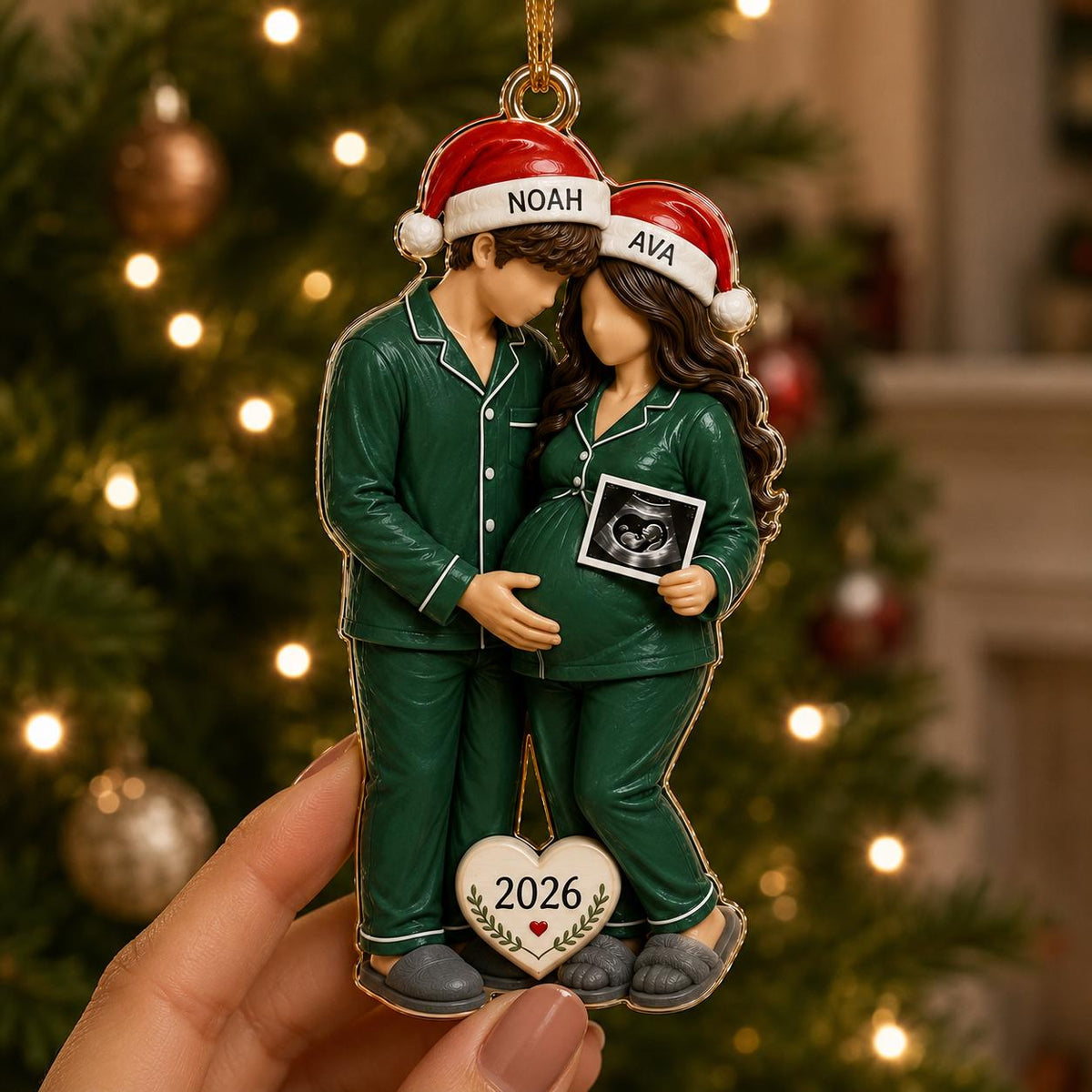 A hanging Christmas ornament featuring two figures in green pajamas and Santa hats labeled NOAH and AVA. The figures stand together, one holding an ultrasound image, with a heart-shaped tag at the bottom displaying the year 2026.