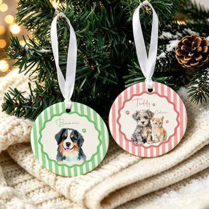 Two round ceramic ornaments with white ribbon hangers. One features green stripes, a scalloped border, and a Bernese Mountain Dog illustration with the name Bean. The other has pink stripes, a scalloped border, and a puppy and kitten with the names Teddy and Caline.