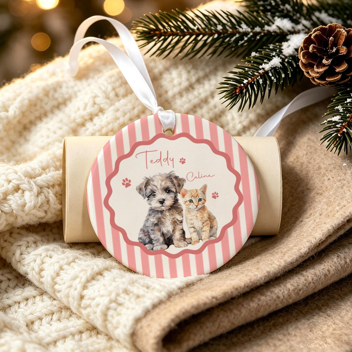 A round ceramic ornament featuring a pink and white striped border and a scalloped center frame. The design displays a watercolor illustration of a small gray puppy and a ginger kitten, with the names Teddy and Celine printed above.