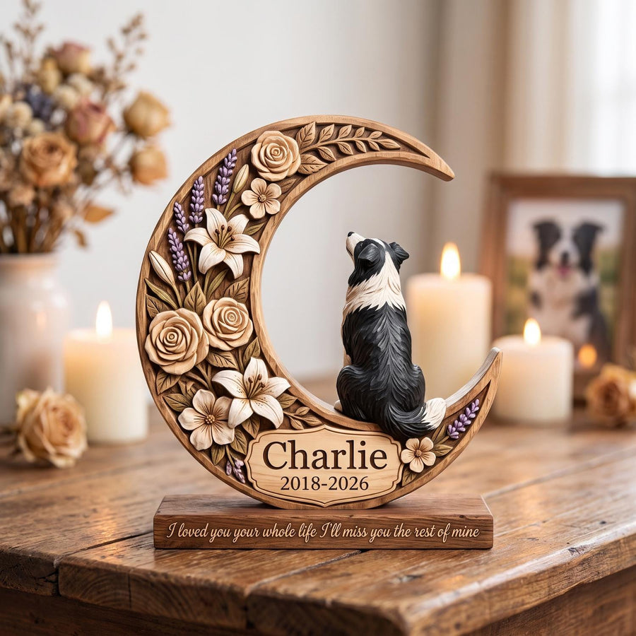 A crescent moon-shaped wooden memorial plaque featuring carved roses and lilies, with a black and white dog figurine sitting on the curve. The plaque displays the name Charlie, the years 2018-2026, and the text I loved you your whole life.