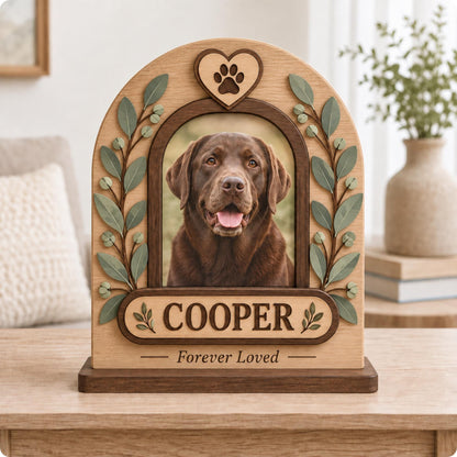 An arched wooden pet memorial frame featuring a central photo of a brown Labrador retriever. The frame is decorated with green leaf accents, a heart with a paw print at the top, and a nameplate with the text COOPER and Forever Loved.