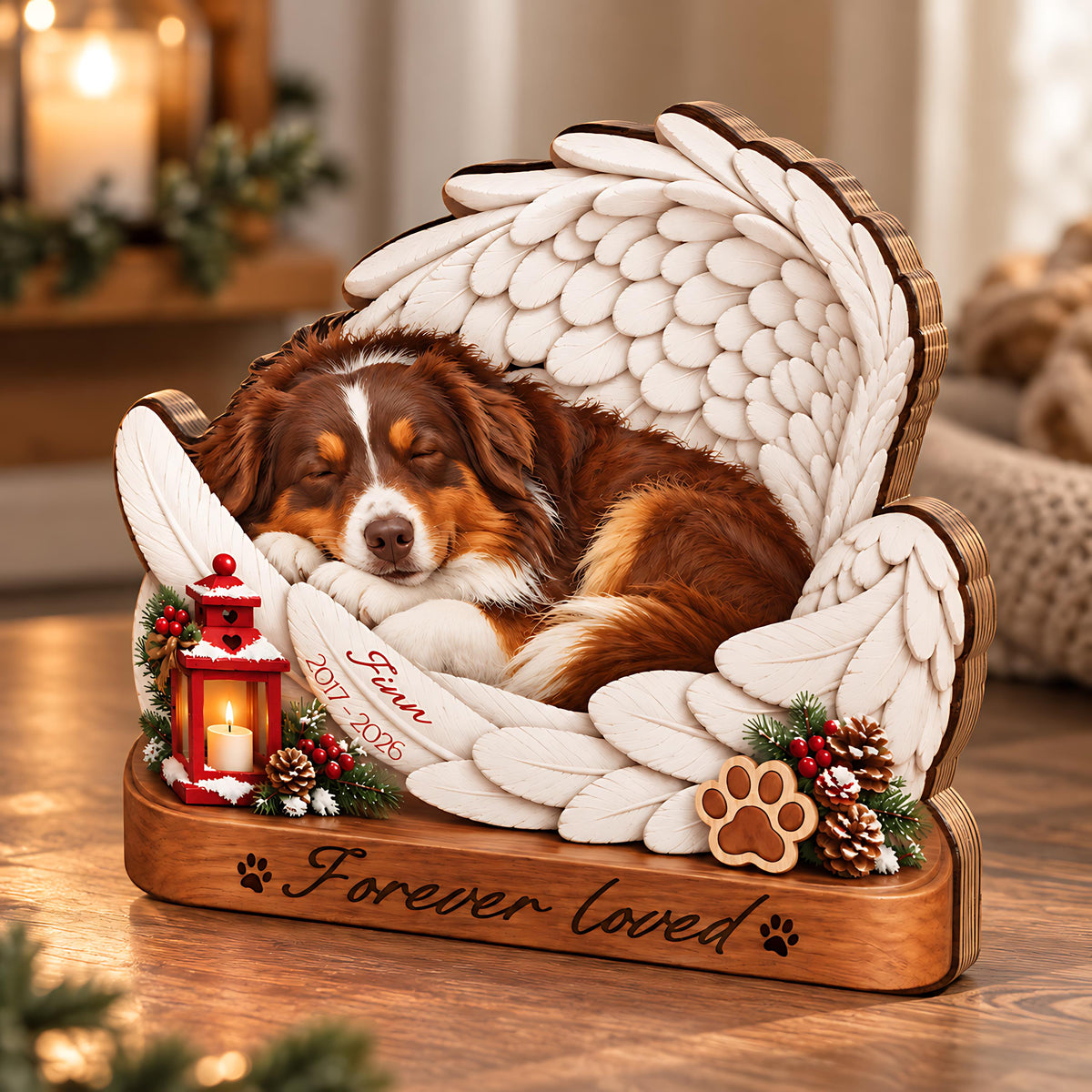 A wooden pet memorial featuring a sleeping brown and white dog nestled within large white angel wings. The base is engraved with "Forever loved" and paw prints. A red lantern, pinecones, and a feather inscribed "Finn 2017-2026" are included.