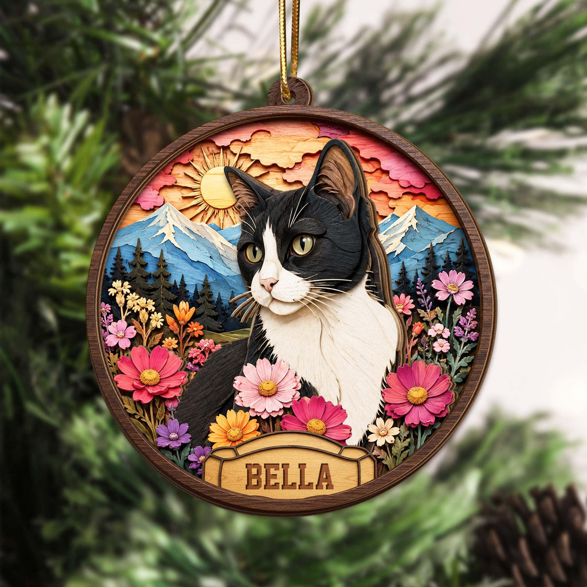 A circular wooden ornament featuring a layered, multi-dimensional scene of a black and white cat. The background displays a sun, mountains, and a forest. The foreground includes colorful flowers and a nameplate with the text BELLA.