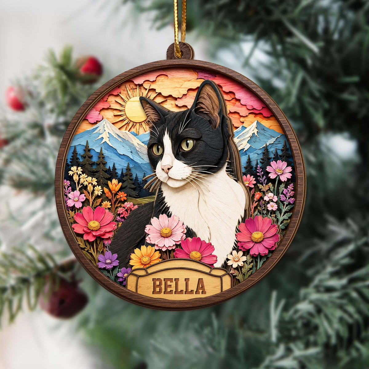 A round wooden ornament featuring a layered 3D-style illustration of a black and white cat surrounded by colorful flowers, mountains, and a sun. A small rectangular plaque at the bottom displays the name BELLA in capital letters.