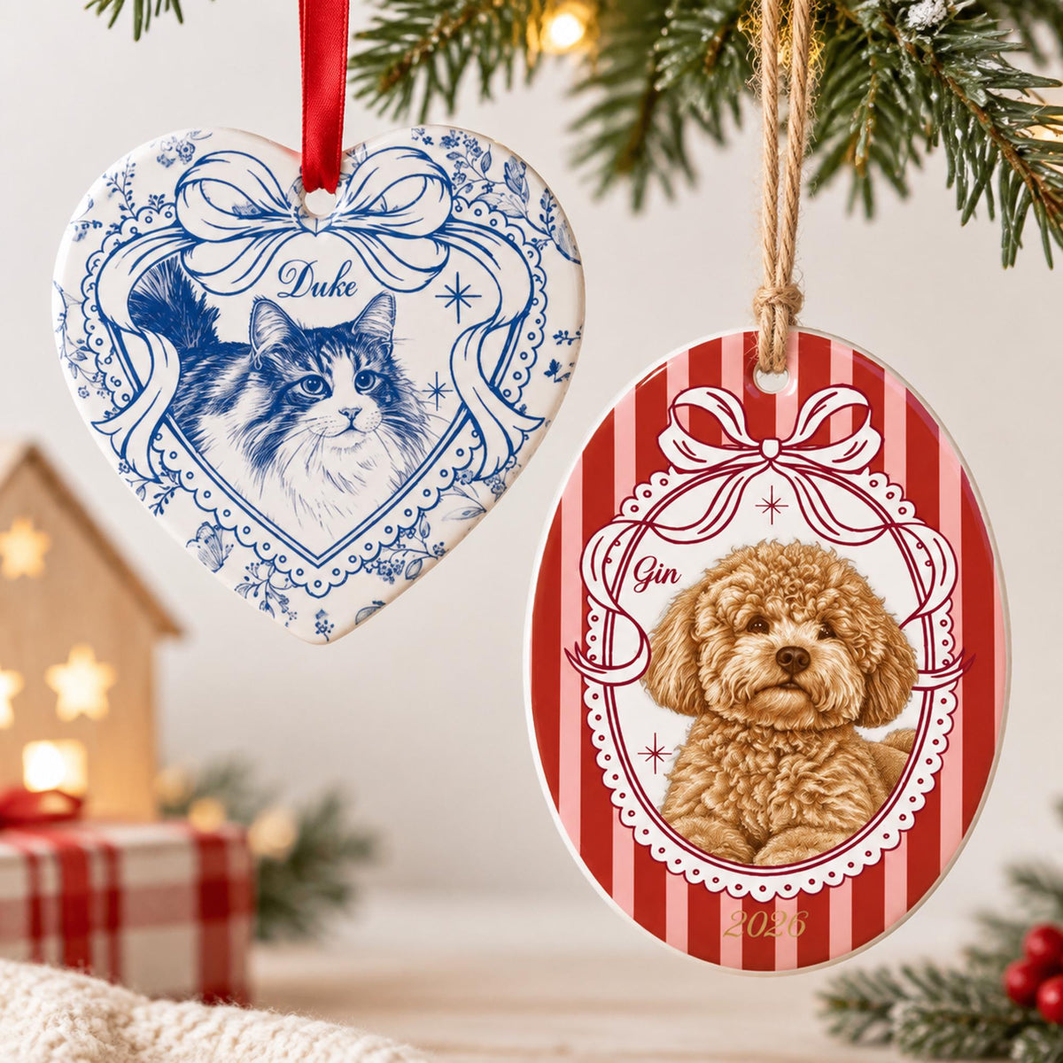 Two ceramic ornaments hanging from strings. One heart-shaped ornament features a blue and white floral border with a cat illustration and the name Duke. The other oval ornament has a red and white striped background with a dog illustration, the name Gin, and the year 2026.