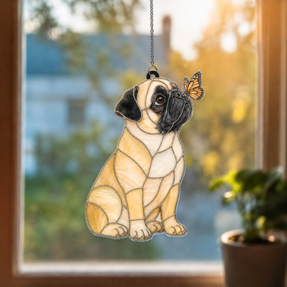 A stained glass suncatcher shaped like a sitting pug dog with light tan fur and a black muzzle. A small orange and black monarch butterfly rests on the dog's nose. The piece is suspended by a thin silver metal chain for hanging.