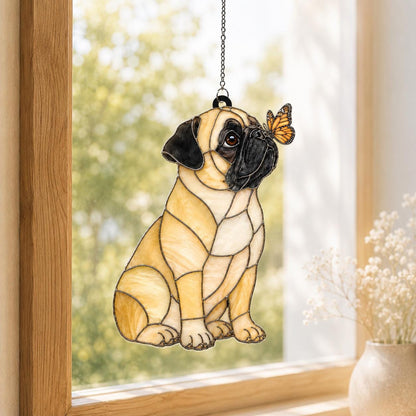 A stained glass suncatcher shaped like a sitting pug dog with tan and black glass segments. The pug has a black muzzle and ears, and a small orange and black monarch butterfly is perched on its nose. It hangs from a metal chain.