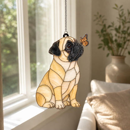 A stained glass suncatcher shaped like a sitting pug dog with tan and black glass pieces. The pug has a small orange and black butterfly perched on its nose. The piece is suspended by a thin metal chain against a bright window.