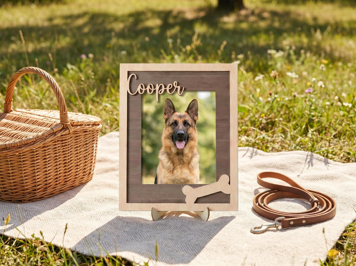 A rectangular wooden picture frame with a light wood outer border and a dark wood inner frame. The name Cooper is written in cursive script at the top, and a light-colored wooden bone shape is attached to the bottom right corner.