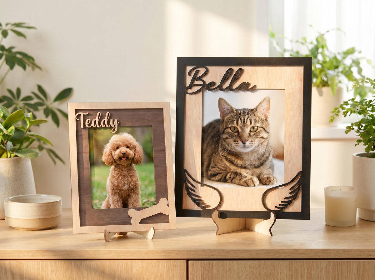 Two rectangular wooden picture frames with stands. The smaller frame features the name Teddy in script and a bone cutout. The larger frame features the name Bella in script and two wing cutouts. Each frame holds a pet photograph.
